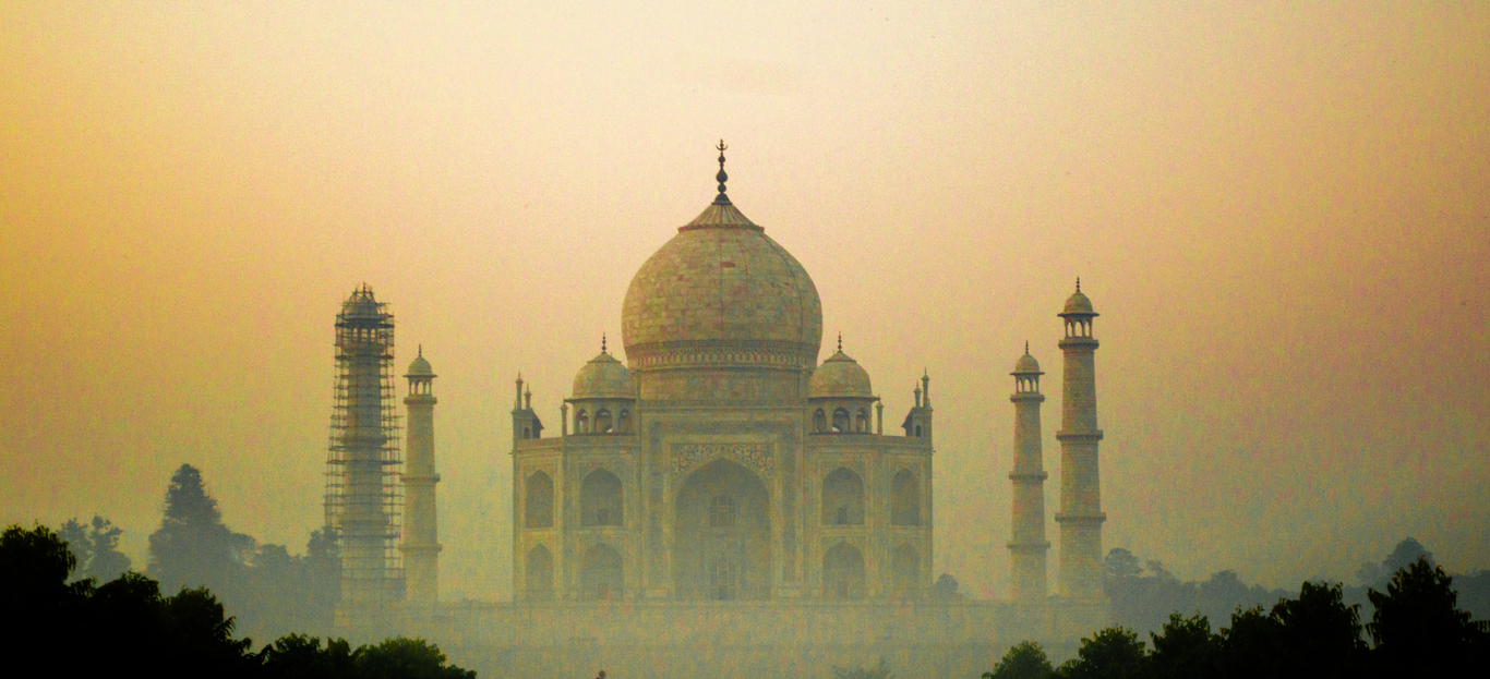 The white marble Taj Mahal mausoleum at dawn with a misty reflection on the Yamuna River in Agra.