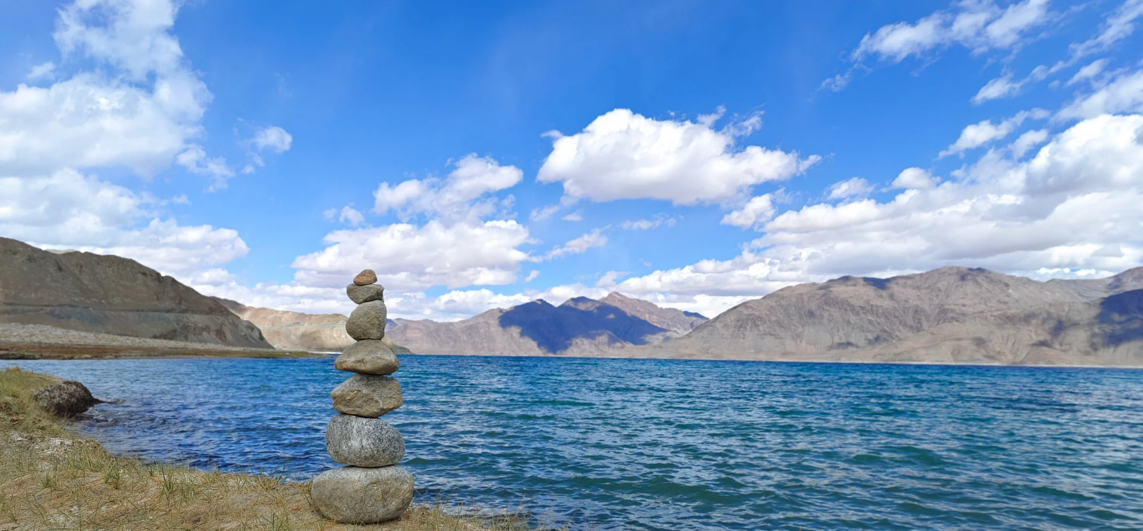 Graceful Tibetan stone stack balanced on the shore of sapphire blue Pangong Lake in Ladakh, India.