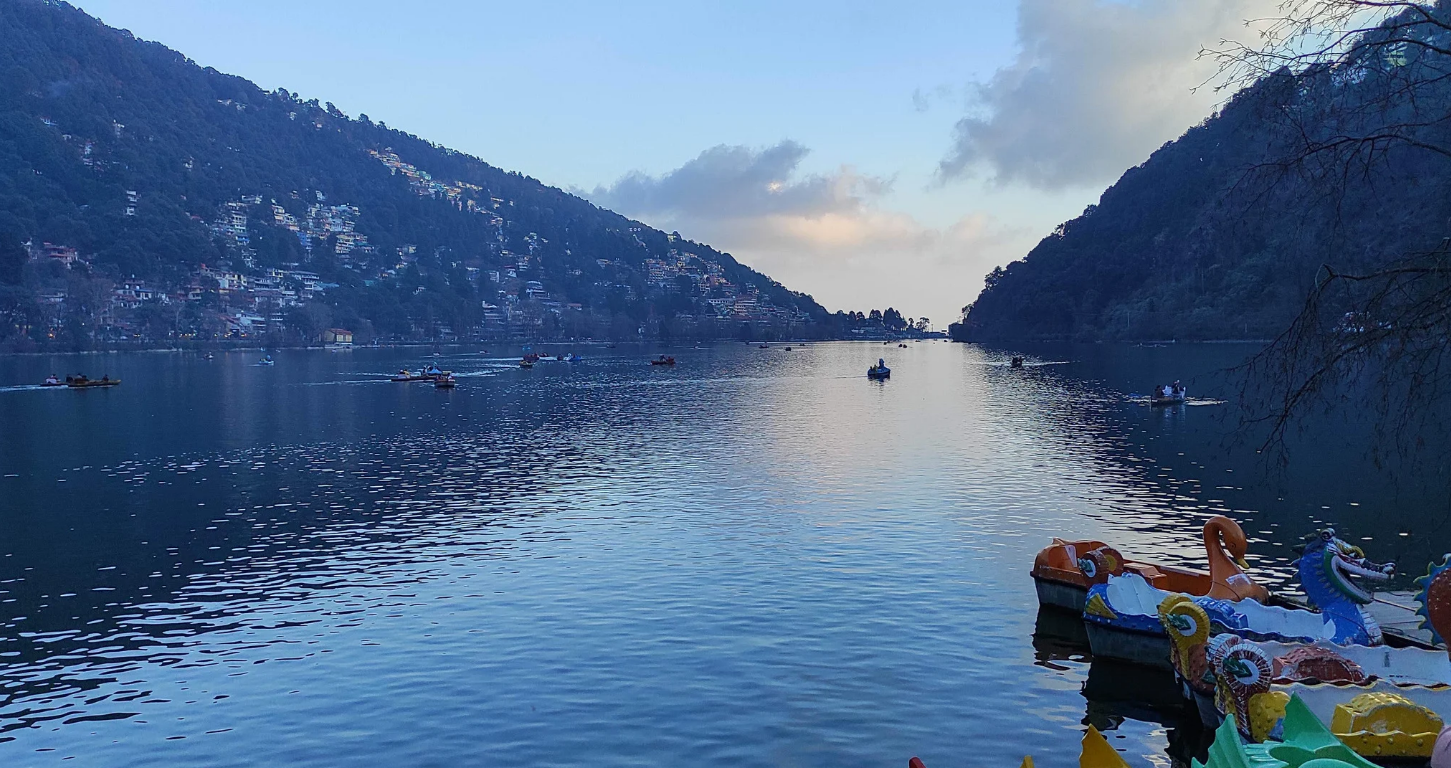 Colorful rowing boats on the emerald-green Naini Lake surrounded by lush Kumaon hills in Nainital, Uttarakhand.